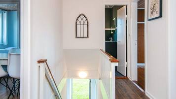 A hallway with a wooden ceiling, a white wall with a window, and a door leading to a room with a dark floor.