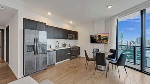 A modern kitchen with a stainless steel refrigerator, dark cabinets, and a large window with a city view. - Spacious Miami 3BR w/ City & Bay Views (Miami)