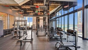 A modern gym with various weightlifting equipment, large windows offering views of the city, and a high ceiling with exposed ductwork. - Spacious Miami 3BR w/ City & Bay Views (Miami)