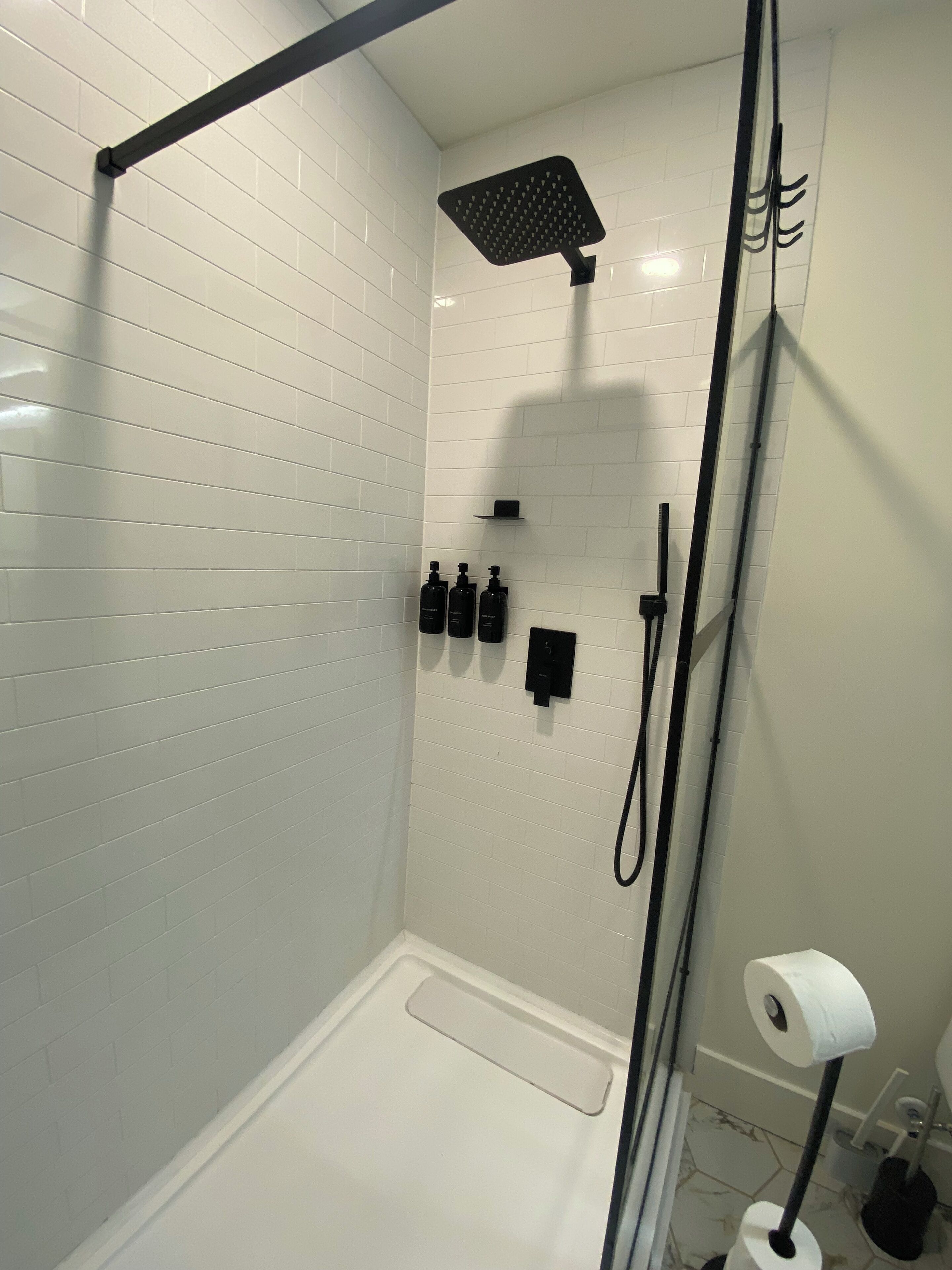 A modern shower with a handheld showerhead, a wall-mounted control panel, and a toilet paper holder.