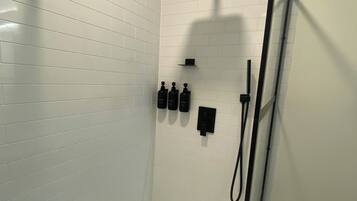 A modern shower with a handheld showerhead, a wall-mounted control panel, and a toilet paper holder.