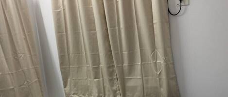 A single bed with a red and white quilted bedspread, beige curtains, and an air conditioning unit mounted on the wall.