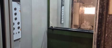 An elevator interior with a control panel, a reflective mirror, and a door with a window.