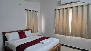 A neatly made bed with a wooden headboard, beige curtains, and an air conditioning unit above. - Rivera Nest (Chennai)