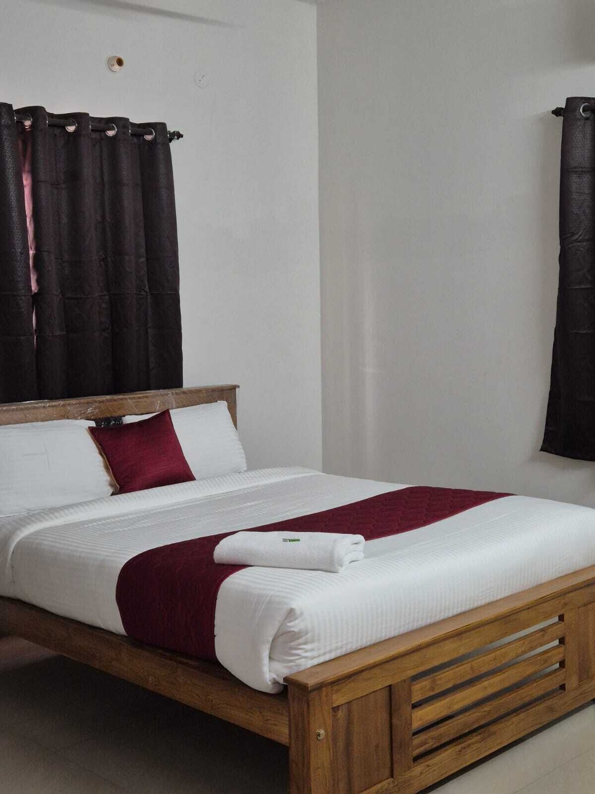 A single bed with a wooden frame, white bedding, and a red throw blanket.