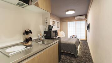 Habitación de hotel compacta con kitchenette, una cama y ventana que proporciona luz natural.
