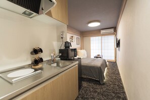 A compact hotel room with a kitchenette, a bed, and a window providing natural light.