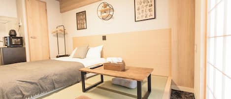 Une chambre d’hôtel bien aménagée, avec un lit, une petite table, un canapé et un futon. Les murs sont décorés et une fenêtre laisse entrer la lumière naturelle.