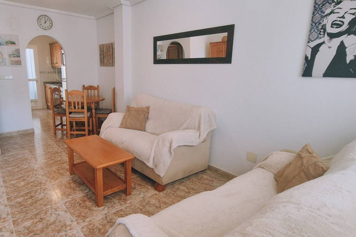 A living room with a sofa, a coffee table, a TV, and a dining area with chairs and a table.