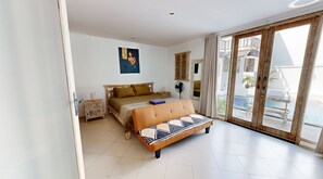 A bedroom with a bed, a nightstand, a fan, and a view of a pool through a sliding door. - Villa Kendal Seminyak (Seminyak)