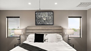 Une chambre à coucher avec un grand lit, deux lampes de chevet, une tête de lit et une œuvre d’art murale.