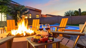 Une terrasse avec un foyer, du mobilier d’extérieur, une piscine et un plateau de fruits accompagné de verres à vin.