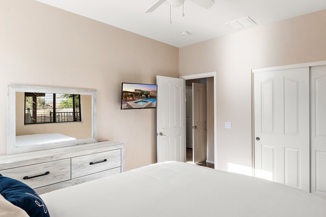 A bedroom with a bed, a dresser, a TV mounted on the wall, and a door leading to another room.