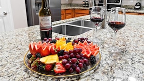 Une assiette de fruits, une bouteille de Bay Bridge Cabernet Sauvignon et deux verres de vin rouge sont posés sur un comptoir de cuisine.