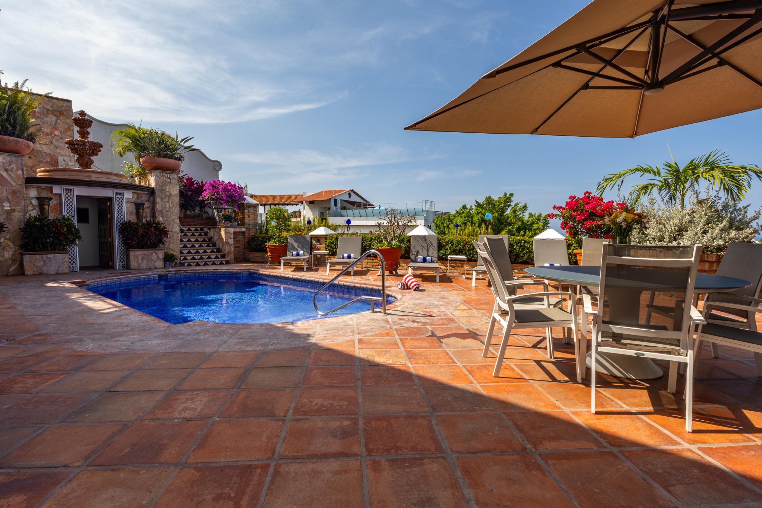 A pool area with tiled flooring, lounge chairs, and umbrellas.
