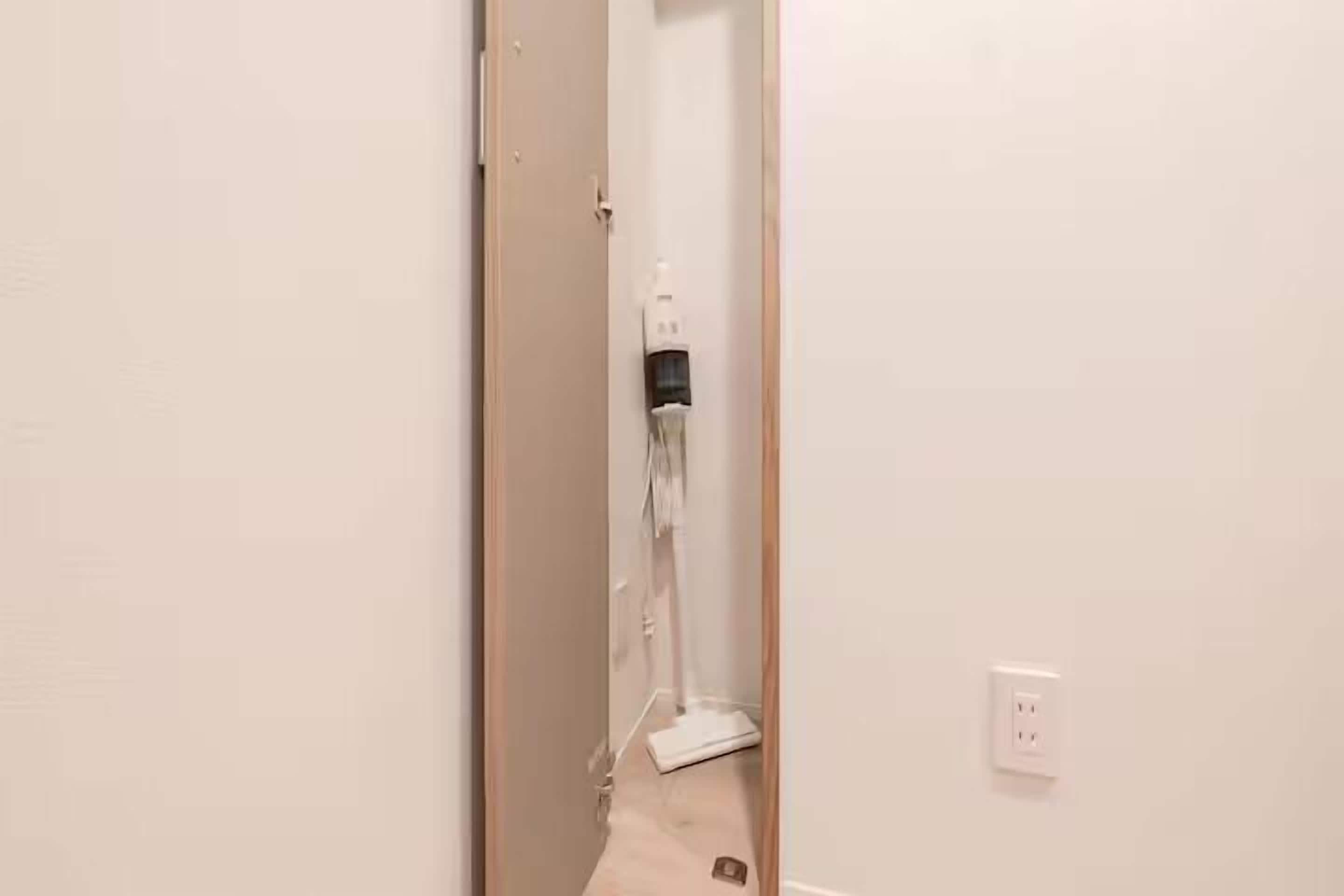 A narrow hallway with a door on the left and a white wall on the right. A white electrical outlet is visible on the wall.