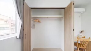 Une pièce de taille modeste avec un plancher en bois, une petite table accompagnée d’une chaise, une armoire et une fenêtre avec des rideaux.