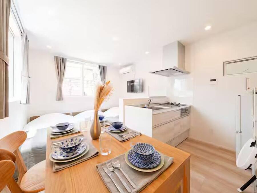 A modern, well-lit room with a dining table set for two, a kitchen area with a microwave and stove, and a large window providing natural light.