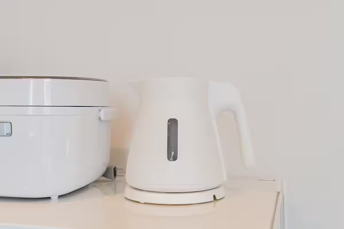 A white electric kettle and a white rice cooker on a white countertop.