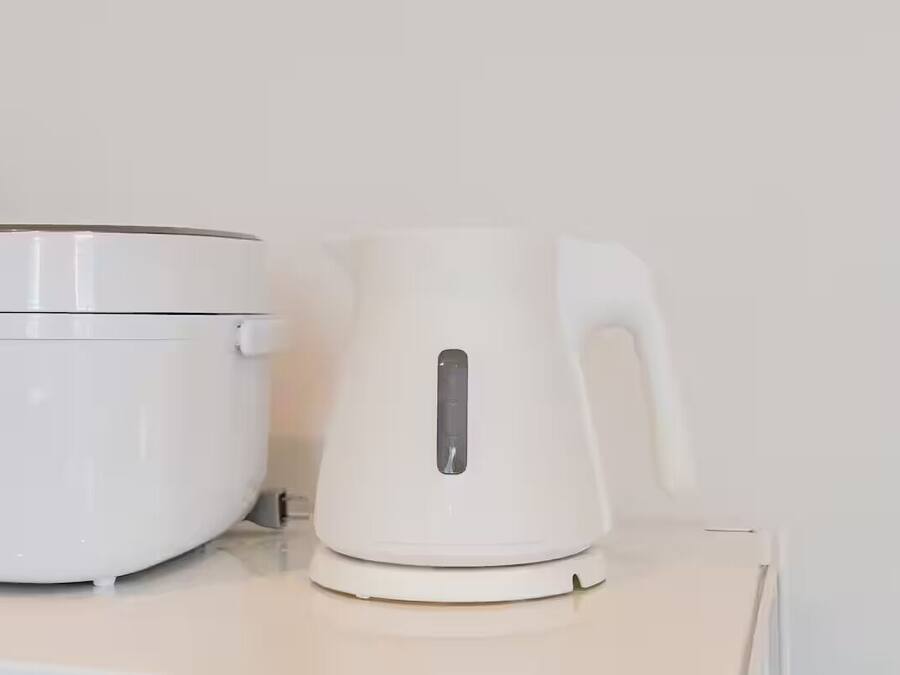 A white electric kettle and a white rice cooker on a white countertop.