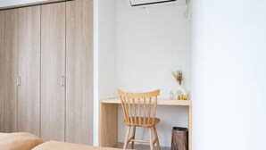 Une chambre à coucher avec une armoire en bois, un bureau avec une chaise et une petite poubelle.