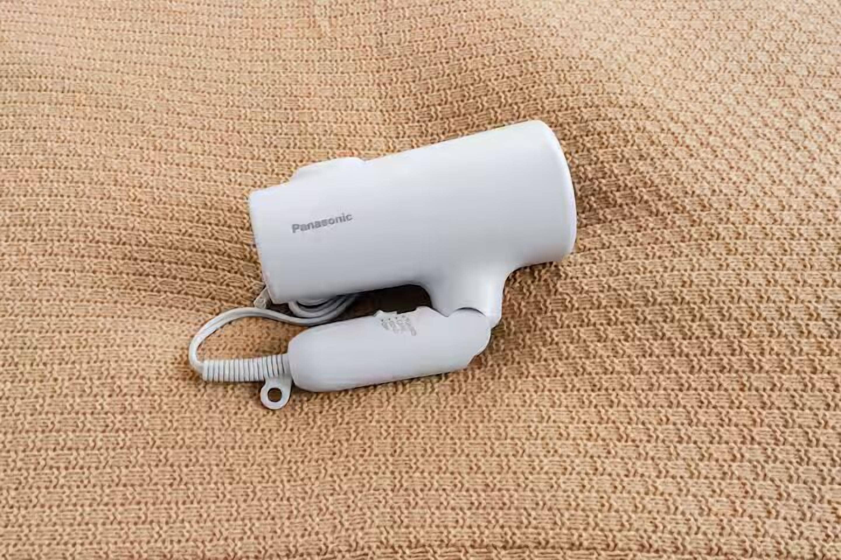 A Panasonic hair dryer on a textured beige surface.