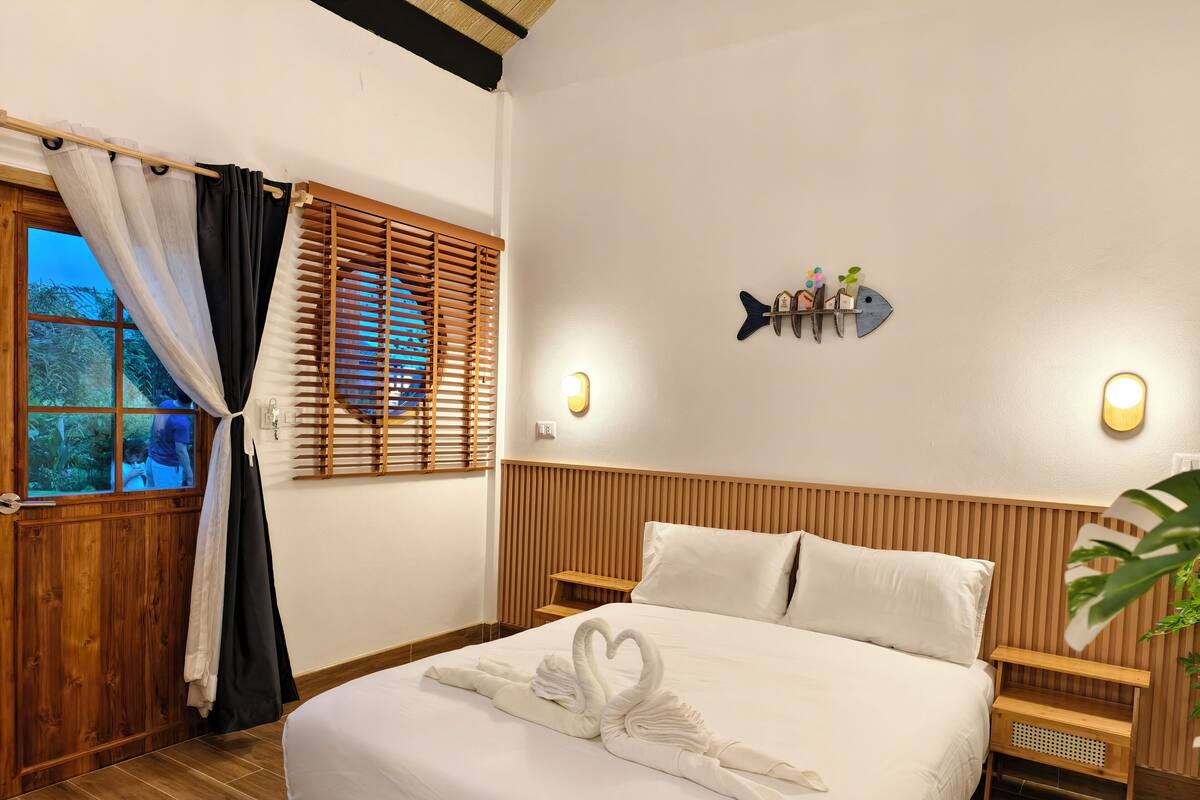 A hotel room with a bed, wooden headboard, wall-mounted light fixtures, and a window with curtains.