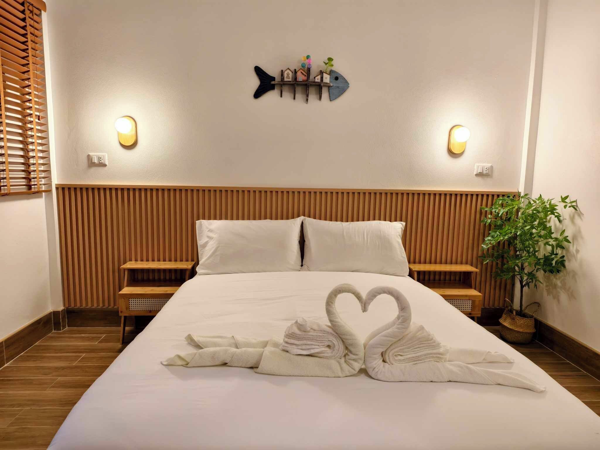 Una habitación de hotel con una cama grande, dos mesitas de noche, una decoración de peces montada en la pared y una planta en maceta.