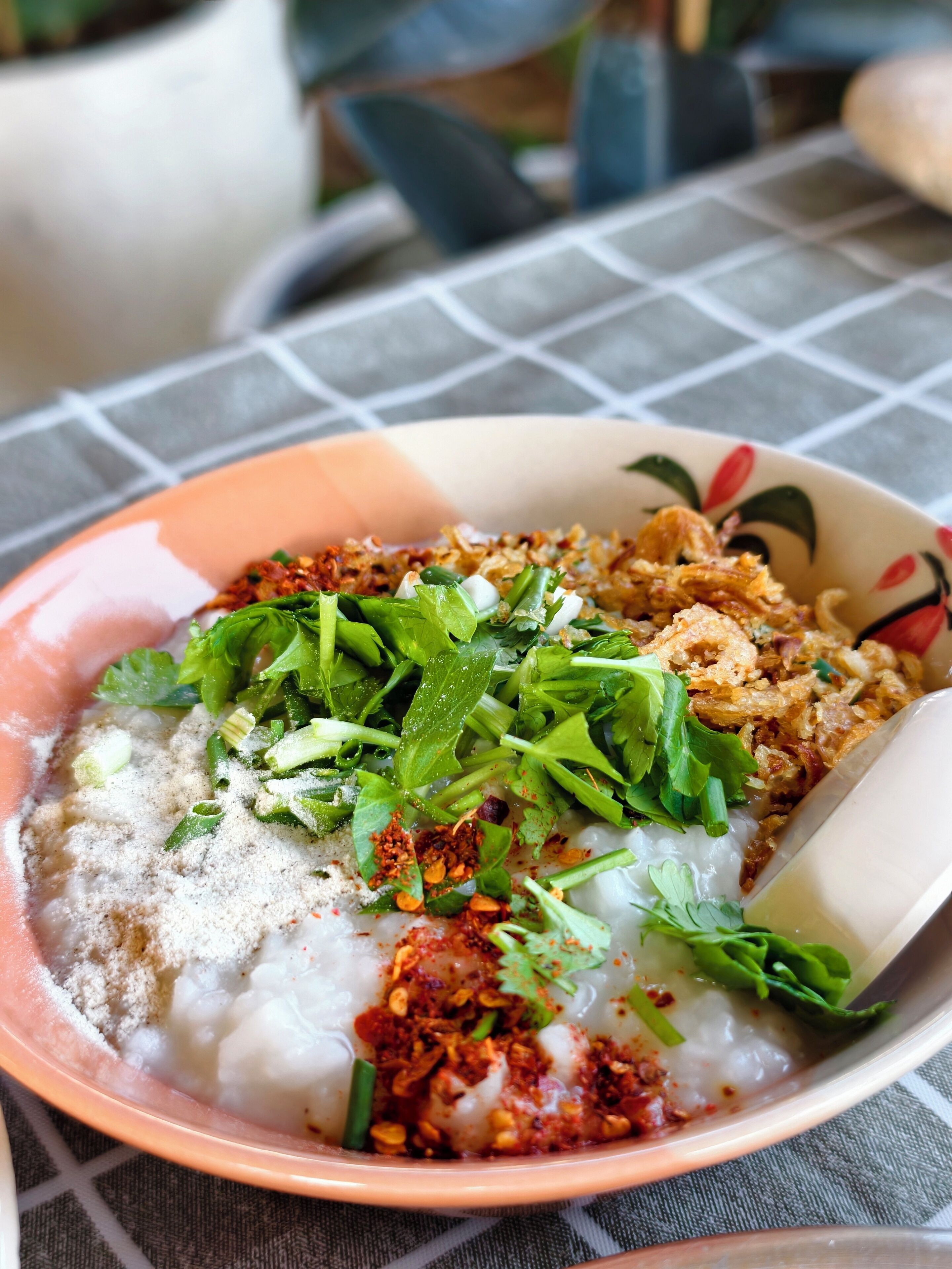 A bowl of rice noodles topped with fried shallots, green herbs, and chili flakes.