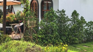 Un bâtiment blanc orné d’un logo vert et d’une inscription en thaï, une pergola en bois couverte de plantes grimpantes et un jardinière en forme de roue de vélo.