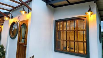 A building with a white exterior, a wooden door, a large window with blinds, and two wall-mounted lights.