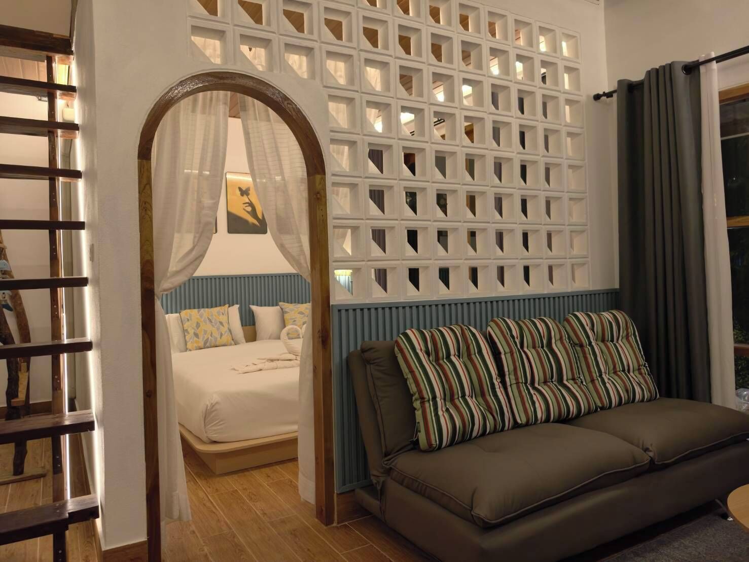A bedroom with a bed, a sofa, a decorative wall, and a window with curtains.