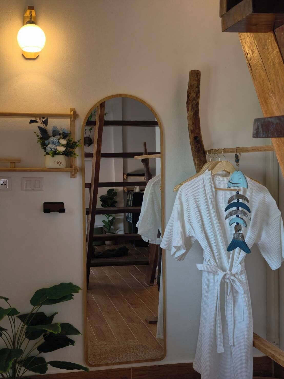 A room with a wooden ladder, a white robe, and a mirror reflecting a staircase.