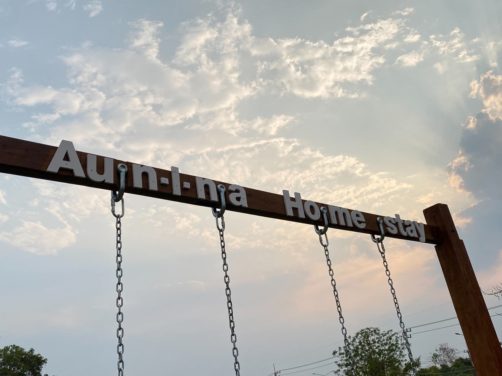 Un letrero con el texto 'Aun-I-nha Home stay' sobre un cielo nublado.