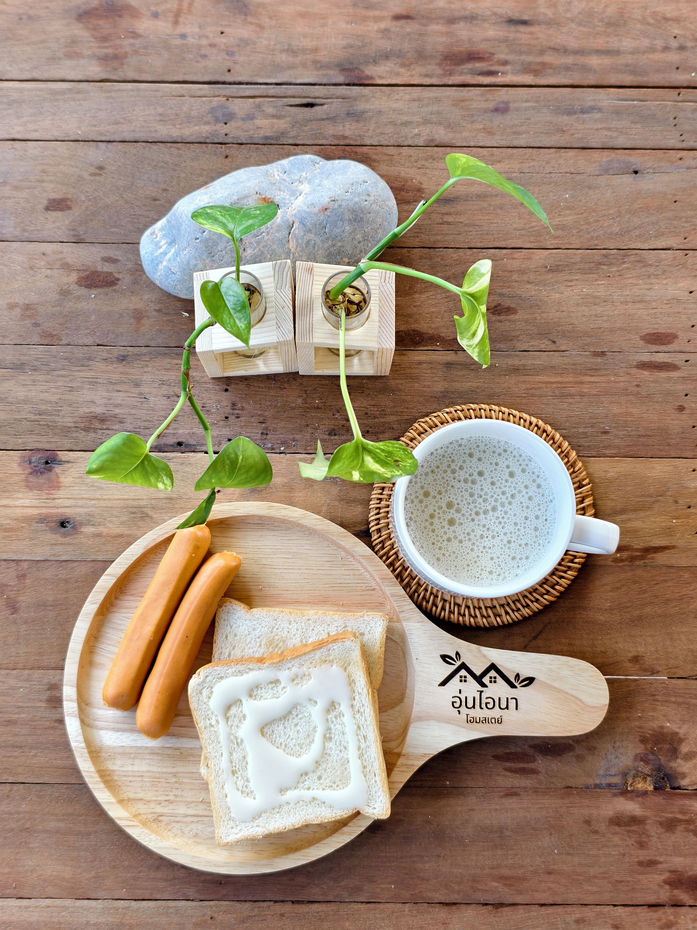 A wooden table with a plate of bread and sausages, a cup of coffee, and a potted plant.