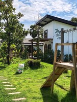 Un jardín con un columpio de madera, una estatua de gato y un edificio con un letrero que dice "Aun-Ima".