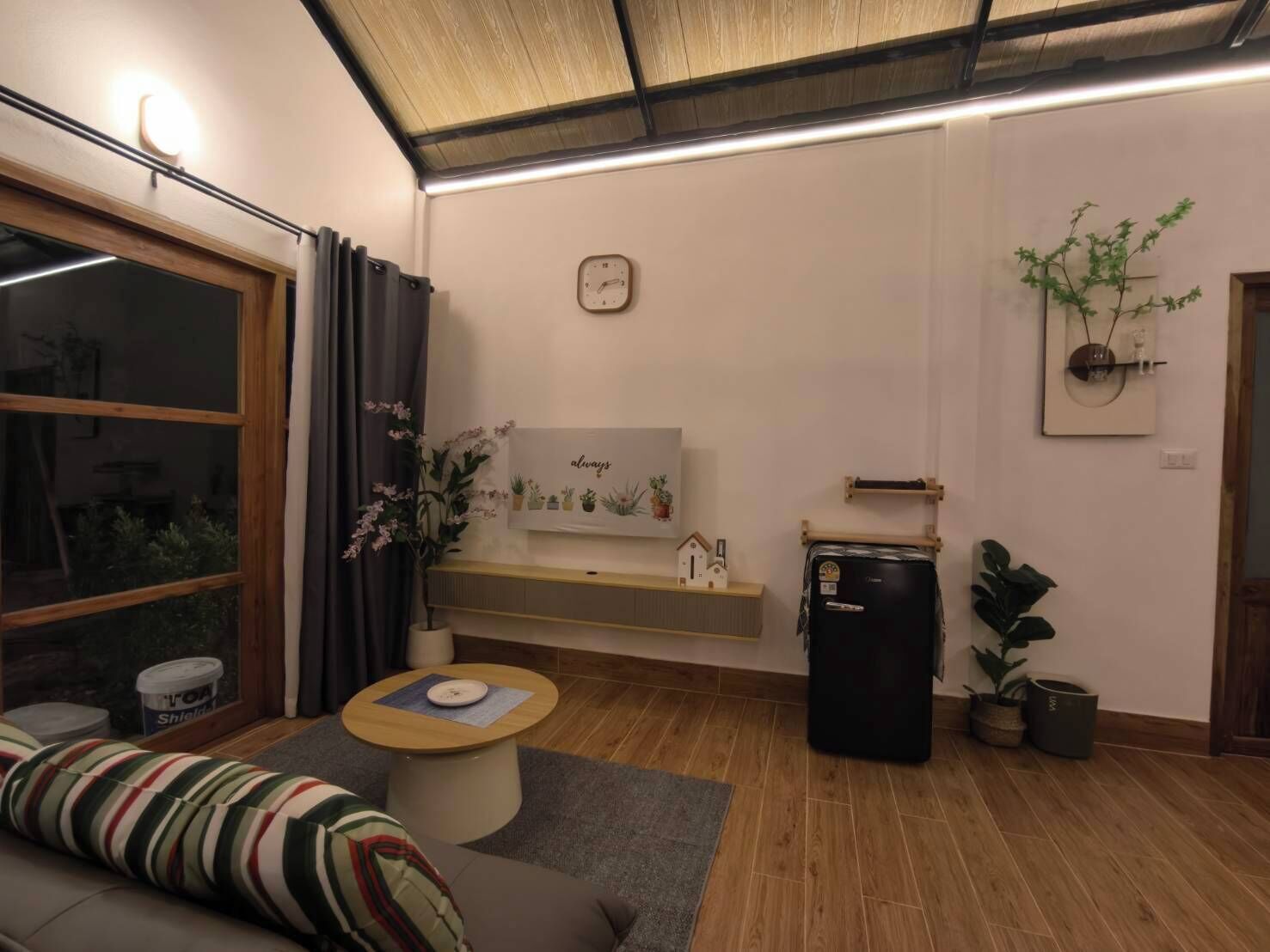Ein Wohnzimmer mit einer Couch, einem kleinen runden Tisch, einer Uhr, einem Heizkörper und einem Blumentopf.