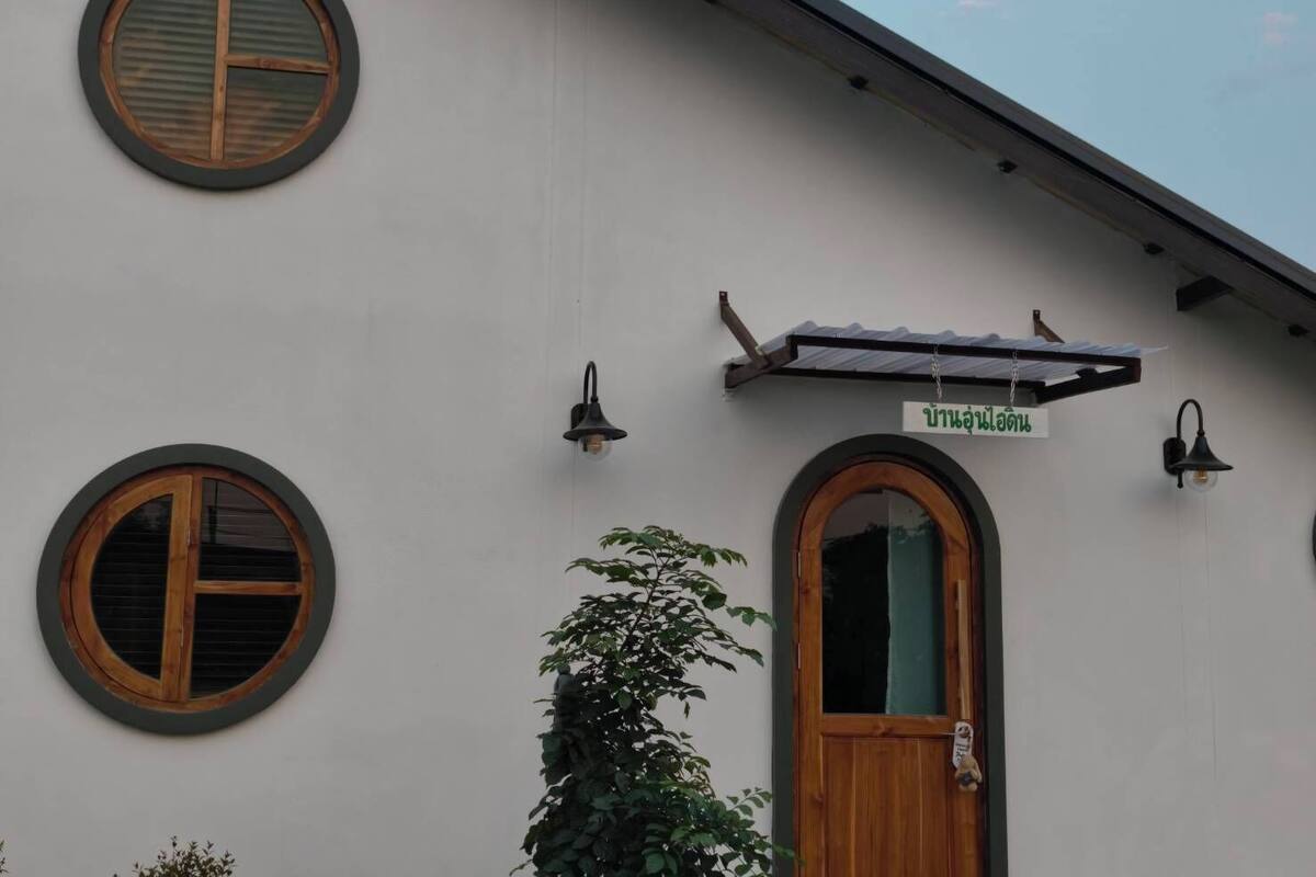 A building with three round windows, a wooden door, and a sign with Thai script.