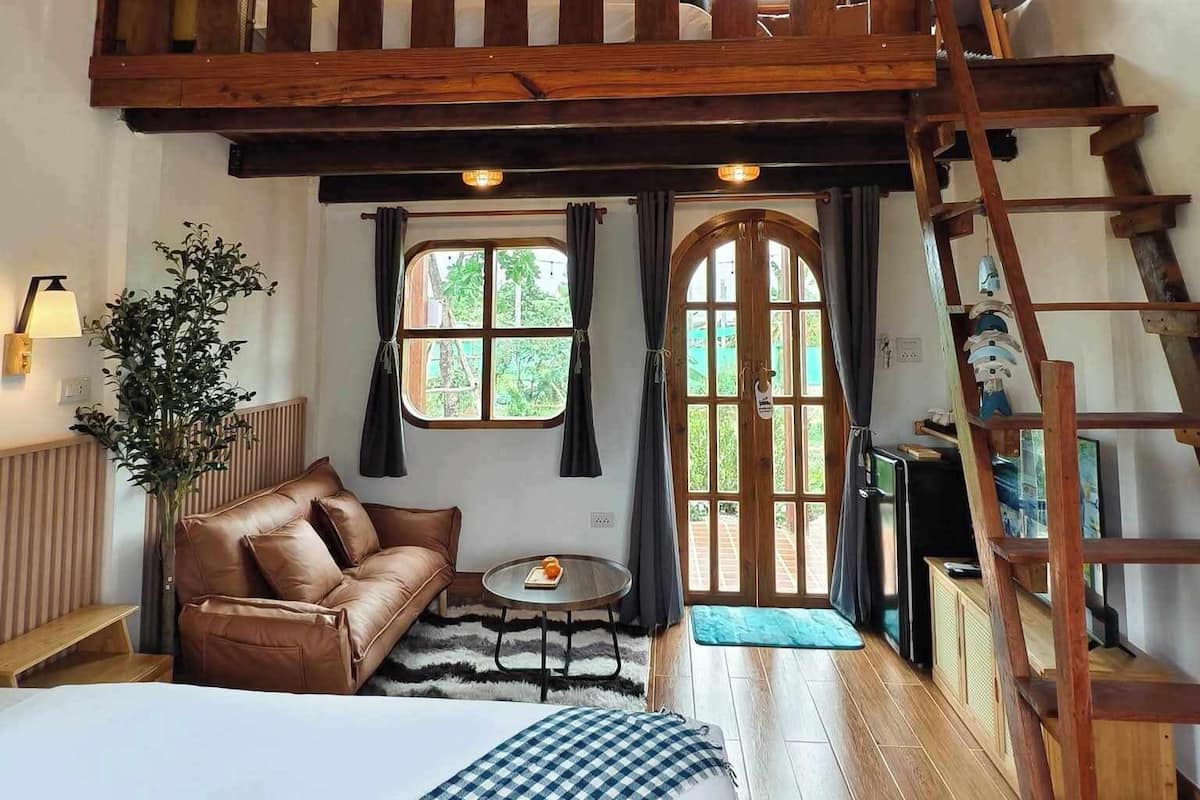 A loft-style bedroom with a large bed, a wooden ceiling, a sofa, a small table, and a ladder.