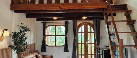 Un dormitorio estilo loft con una cama grande, techo de madera, un sofá, una mesita y una escalera.