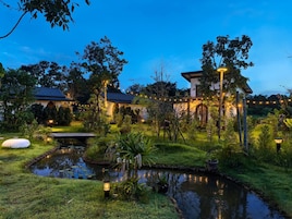 Un jardín tranquilo con un estanque, luces colgantes y un edificio tradicional con techo de tejas.
