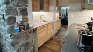 A kitchen with a stone wall, wooden cabinets, a countertop, a toaster, and a sink.