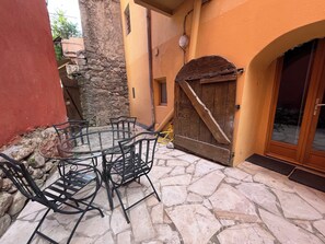 Une terrasse en pierre avec une table en verre et des chaises en métal, une porte en bois et un mur en pierre.