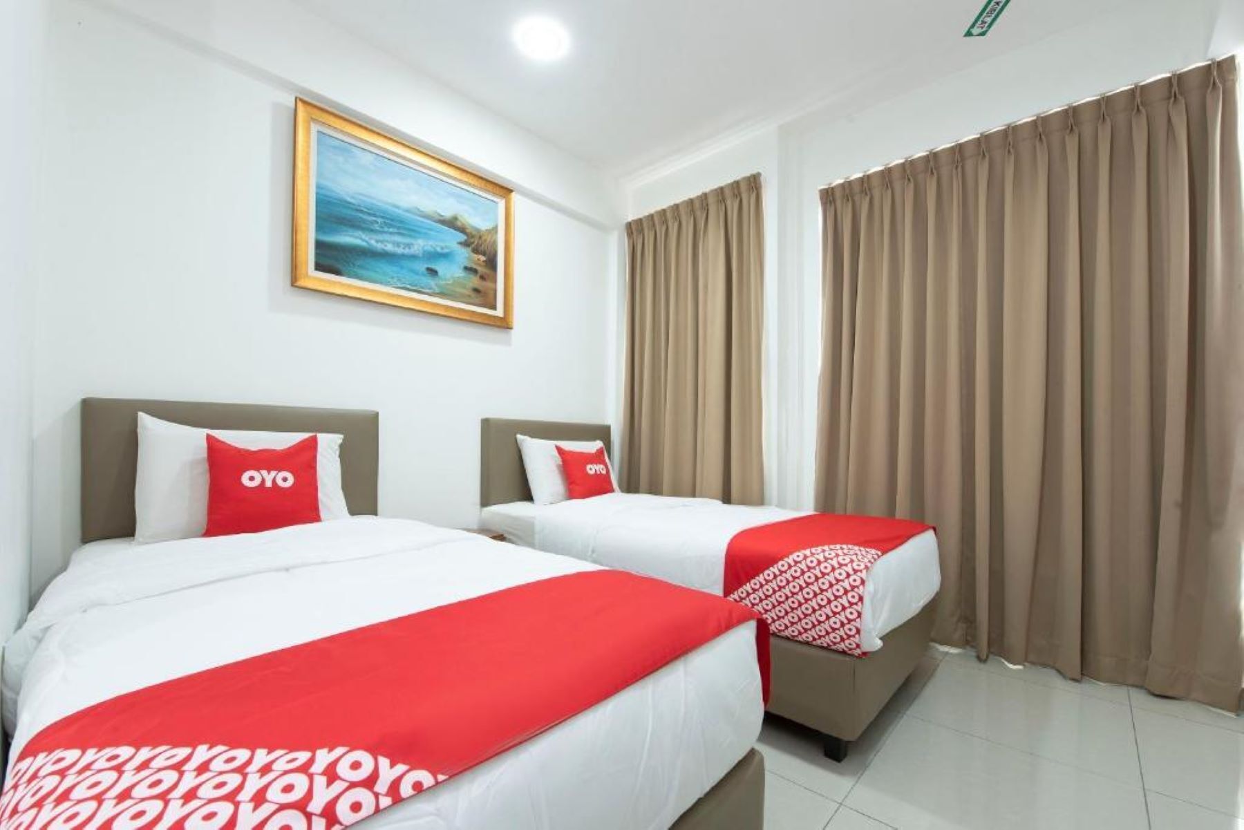 Habitación de hotel con dos camas, cortinas color beige, un cuadro de una playa y una colcha de cama rojo y blanco.