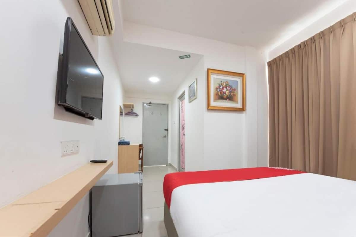 Habitación de hotel con cama, televisor montado en la pared, un escritorio pequeño, refrigerador y puerta que da a un baño.