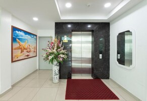 A modern elevator with a marble wall, a red carpet, and a floral arrangement.