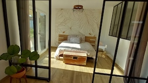 A bedroom with a bed, a bedside table, a potted plant, and a large window.