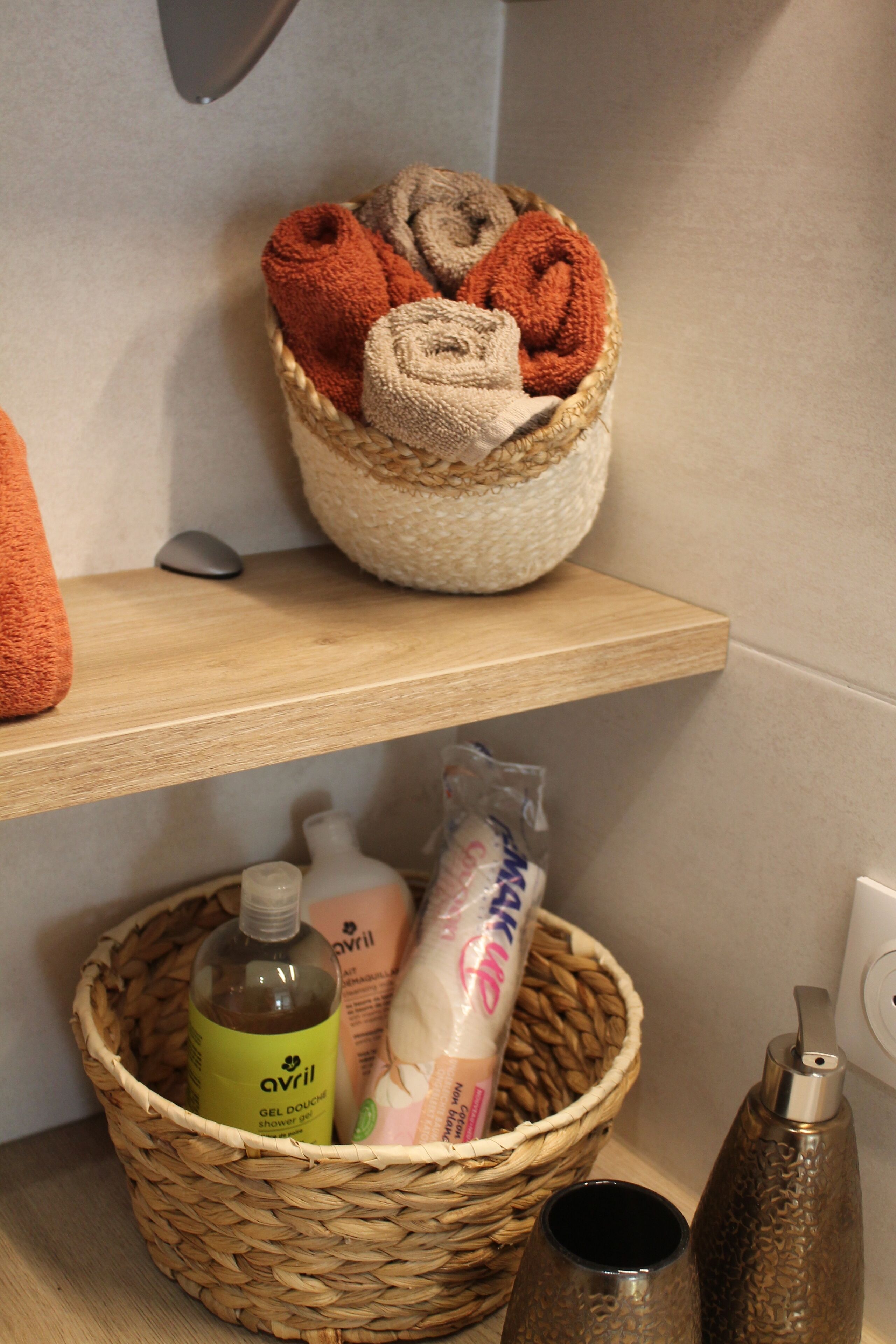 A bathroom shelf with a basket containing rolled towels and toiletries.