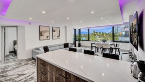 A modern kitchen with a large island, a dining area with a view, and a living space with a sofa and artwork. - Luxury Beachside 3BR/3BA Condo + Resort Amenities, Pools, Gym and Sauna 620 (Miami Beach)