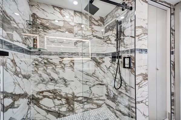 Une douche moderne dotée d’une porte en verre, de murs en marbre et d’un pommeau de douche à main.